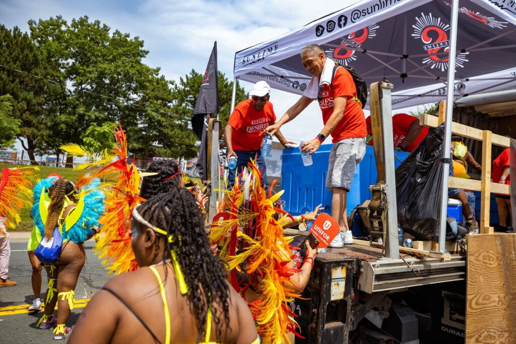 Sunlime team members serving masqueraders water at the 2023 Toronto Caribbean Carnival Parade. Register to play mas with Sunlime Mas at Caribana.